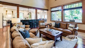 A spacious living room with leather sofas, a coffee table, and a view of the kitchen and dining area. - 6 bed 4 bath cottage on Lake Muskoka, Private, Boathouse, Hot tub! (Gravenhurst)