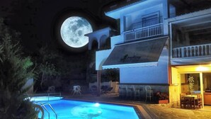 A pool area with a moonlit sky, a building with a balcony, and outdoor seating. - Melissa Gold Coast (Polygyros)