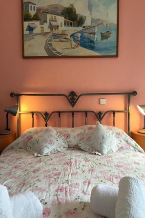 A bed with floral bedding, a painting of a coastal scene, and a metal headboard.