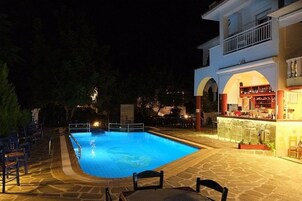 Piscina com deck de pedra, área de bar e mesas ao ar livre.