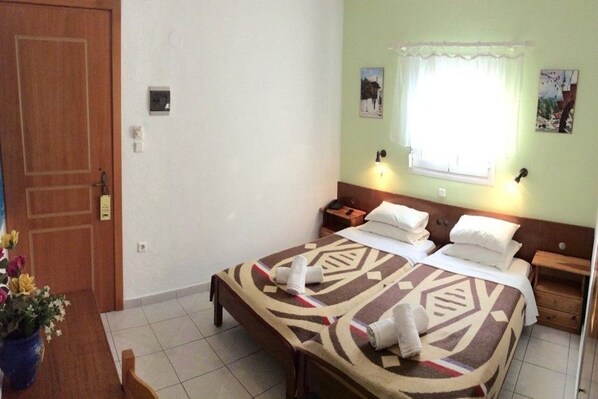 A hotel room with a bed, bedside tables, a window with curtains, and a door.
