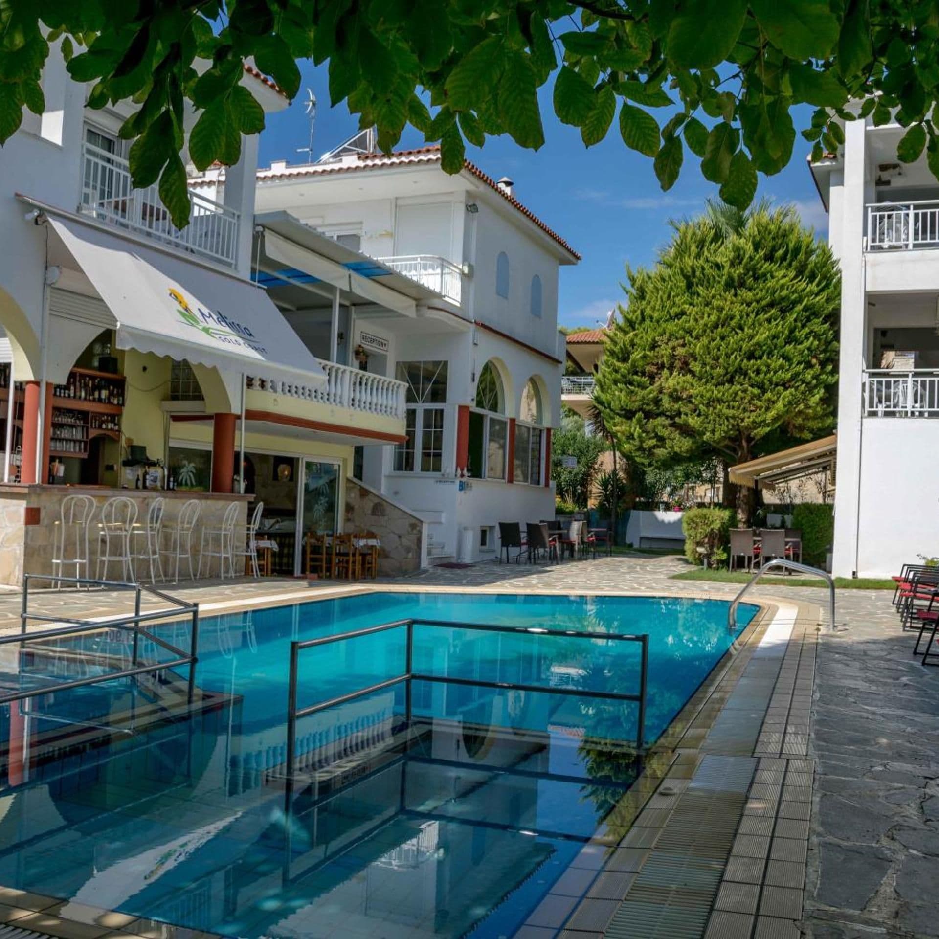 Un área de piscina con una piscina azul cristalina, un espacio de descanso cubierto y un edificio con balcón.
