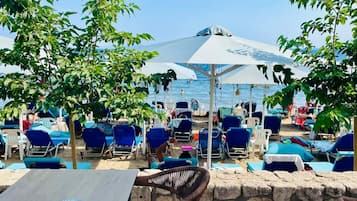 Un área de estar al aire libre con sillones azules y sombrillas, un muro de piedra y vistas a la playa.