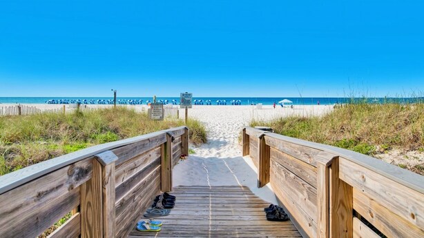 A wooden boardwalk leading to a beach with umbrellas and a clear blue sky. - The Palms 215B | Spacious, recent updates, beach front! (Orange Beach)