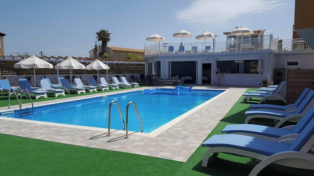 A swimming pool with sun loungers and umbrellas, surrounded by a building with a balcony. - Roda Pearl Resort (Corfu)