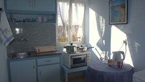 A kitchen with a stove, sink, and window. There is a table with a pitcher and cups. - Roda Pearl Resort (Corfu)