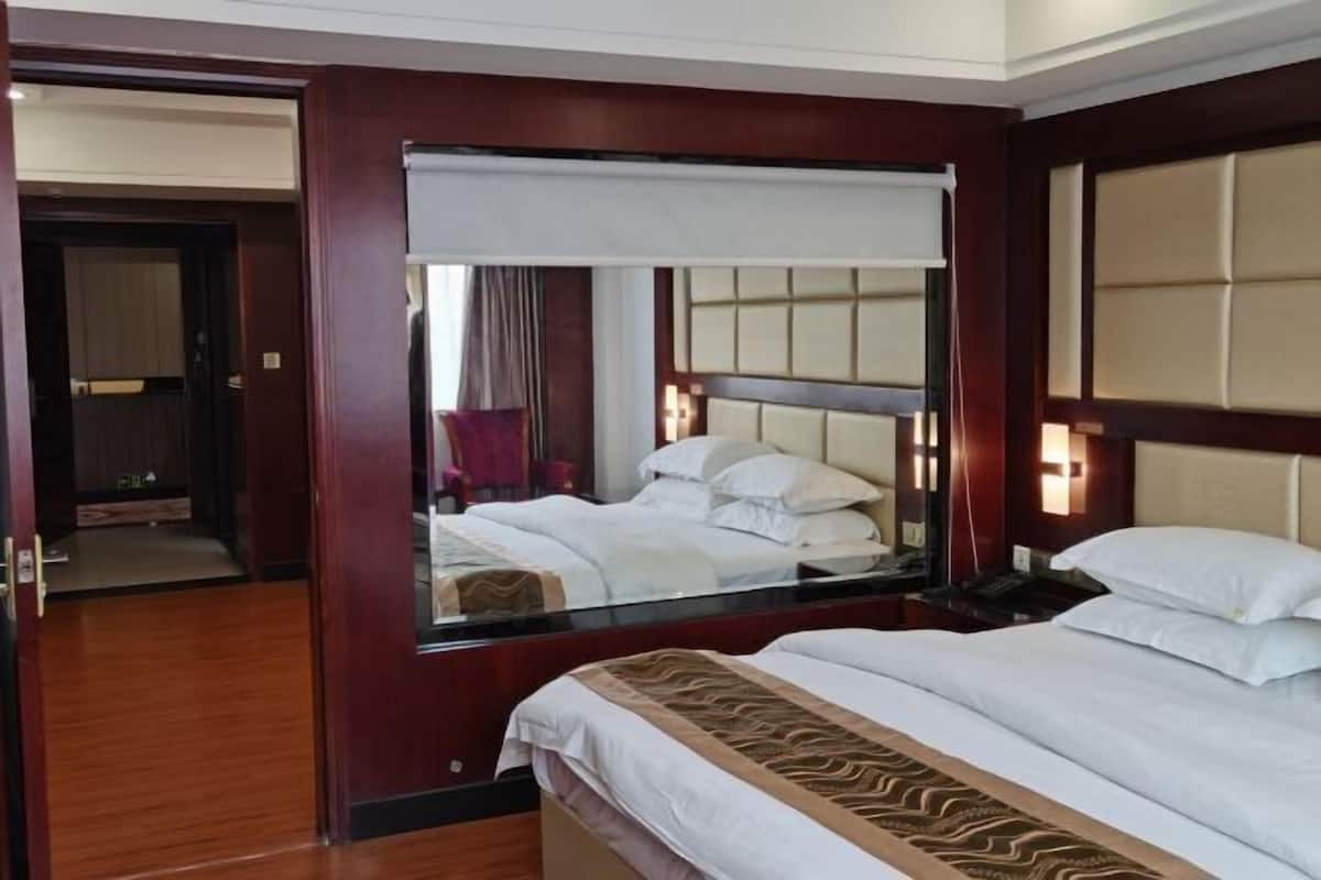 A hotel room with a large bed, a mirror, a nightstand, and a wooden door.