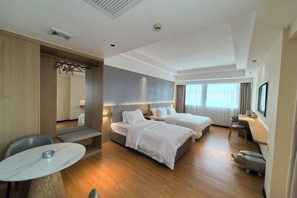 A hotel room with two beds, a desk, a chair, and a TV.