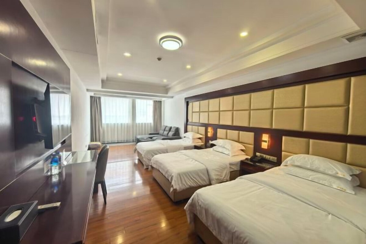 A hotel room with two beds, a desk, a TV, and a window with curtains.