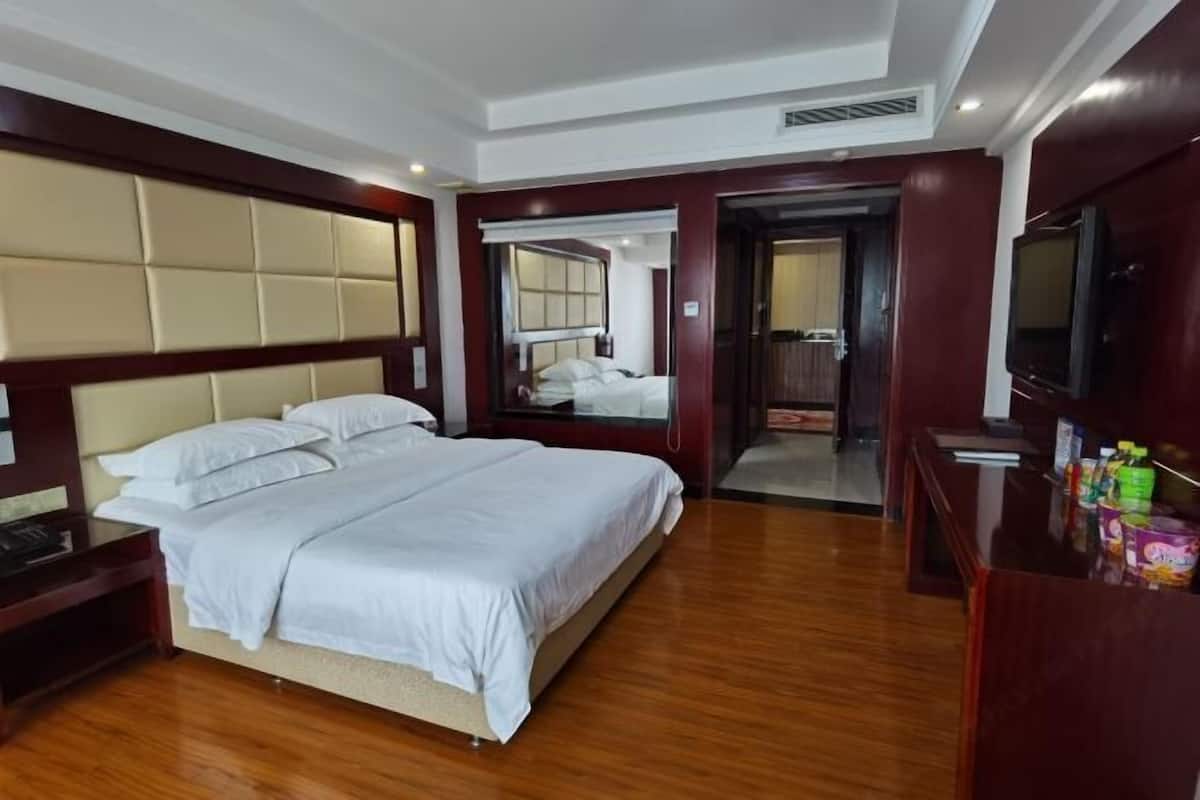 A hotel room with a large bed, a wooden floor, a television, and a minibar.