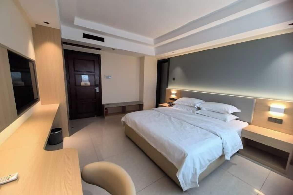 A modern hotel room with a bed, bedside tables, a desk, and a TV.
