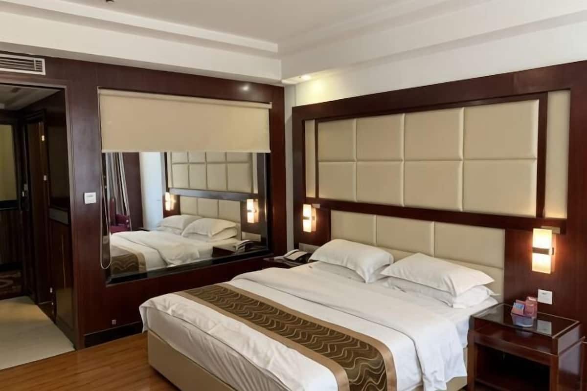 A hotel room with a large bed, a mirror, a nightstand, and a bedside table.