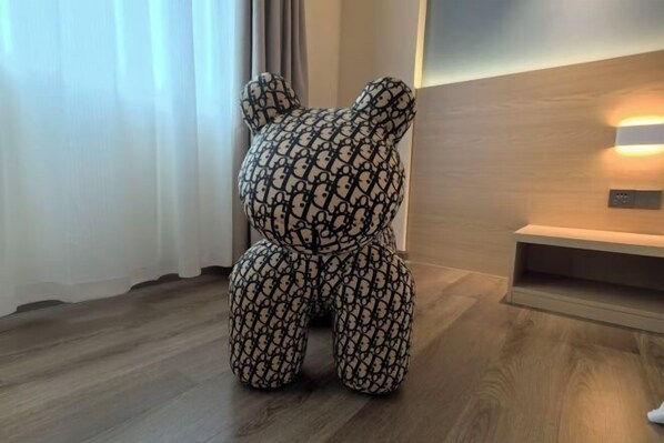 A room with a wooden floor, a bear-shaped cushion, a wall-mounted light, and a small shelf. - Shunde Yufeng Hotel (Foshan)