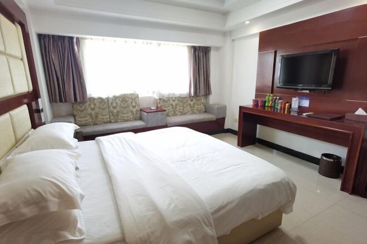A hotel room with a large bed, a sofa, a TV, and a small table with items on it.