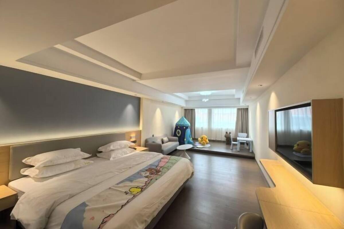 A modern hotel room with a large bed, a desk, a small seating area, and a TV.