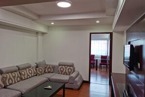 A living room with a sectional sofa, a coffee table, and a flat-screen TV. - Shunde Yufeng Hotel (Foshan)