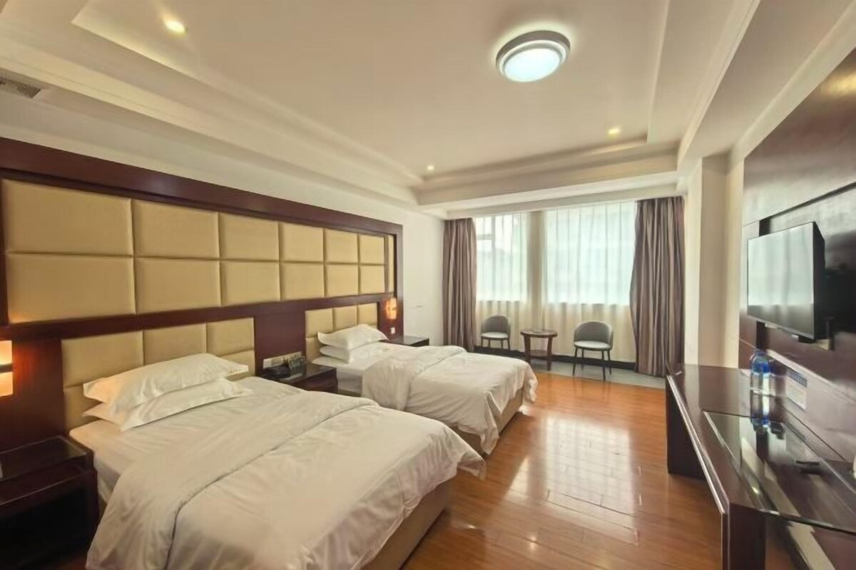 A hotel room with two beds, a TV, a desk, and a window with curtains.