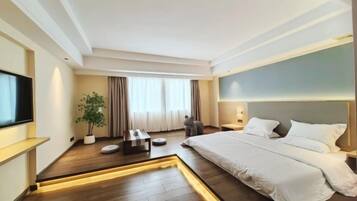 Een moderne hotelkamer met een groot bed, een flatscreen televisie, een potplant en een klein zithoekje.