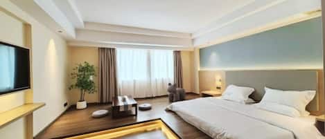 A modern hotel room with a large bed, a flat-screen TV, a potted plant, and a small seating area.