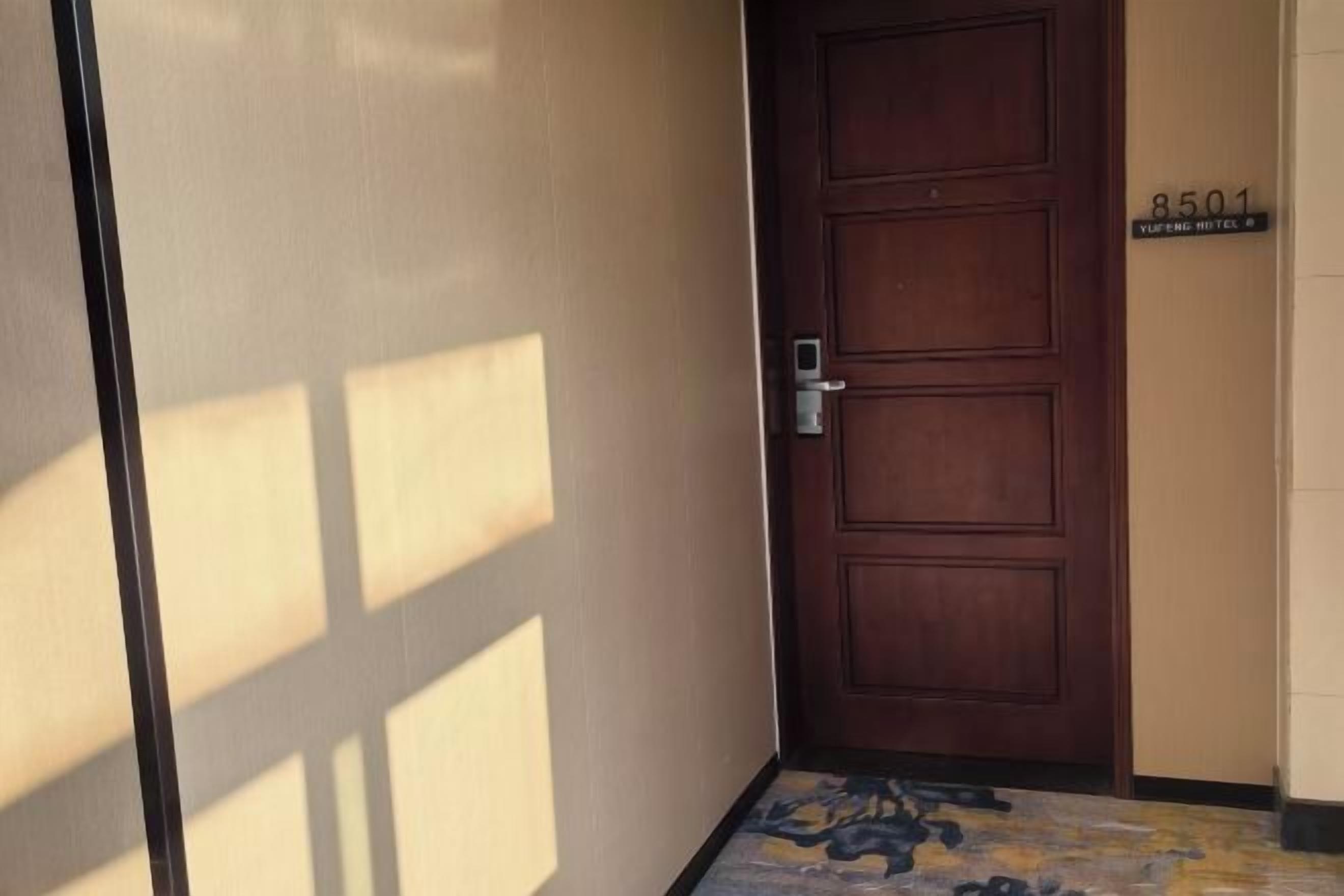 A wooden door with a keypad lock, a number plaque, and a patterned floor mat.