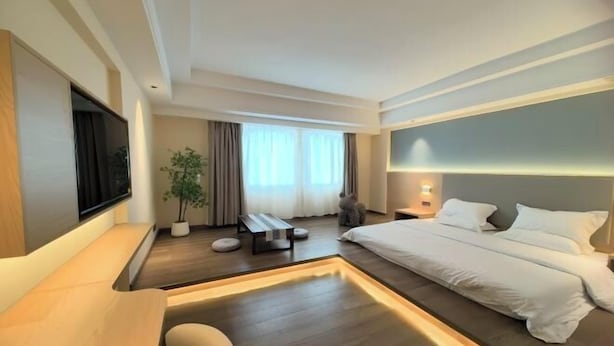 A modern hotel room with a large bed, a desk, a chair, a TV, and a potted plant. - Shunde Yufeng Hotel (Foshan)