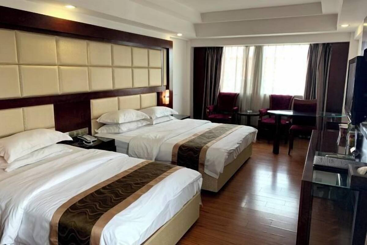 A hotel room with two beds, a TV, a desk, and a chair.