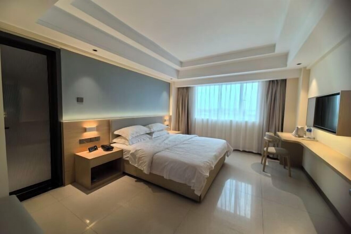 A hotel room with a bed, bedside table, desk, chair, and a TV.