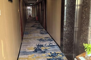A hotel corridor with a carpeted floor, doors on both sides, and a plant on the right. - Shunde Yufeng Hotel (Foshan)
