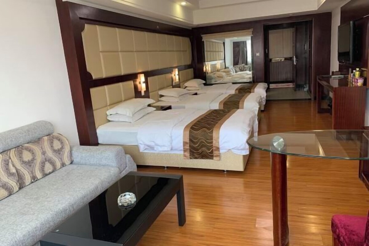 A hotel room with a sofa, a glass table, and a bed with multiple pillows and a blanket.