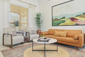 A living room with a sofa, two armchairs, a coffee table, a bookshelf, a potted plant, and a painting on the wall.