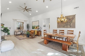 A spacious living room with a wooden dining table, comfortable seating, and a large painting on the wall.