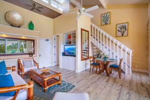 Relax in this spacious living area with a high ceiling and ceiling fan. Enjoy the view of lush greenery from the large window and dine at the table with chairs.
