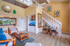 Relax in this spacious living area with a high ceiling and ceiling fan. Enjoy the view of lush greenery from the large window and dine at the table with chairs.