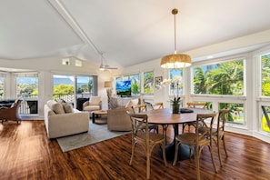 A spacious living area with a dining table, sofas, and a TV. Large windows offer views of greenery and mountains. - Mountain & Waterfall Views - Pool & BBQ (Princeville)
