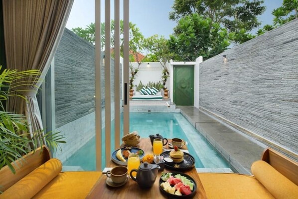 Relax by the serene pool surrounded by lush greenery, with a seating area for a peaceful breakfast.