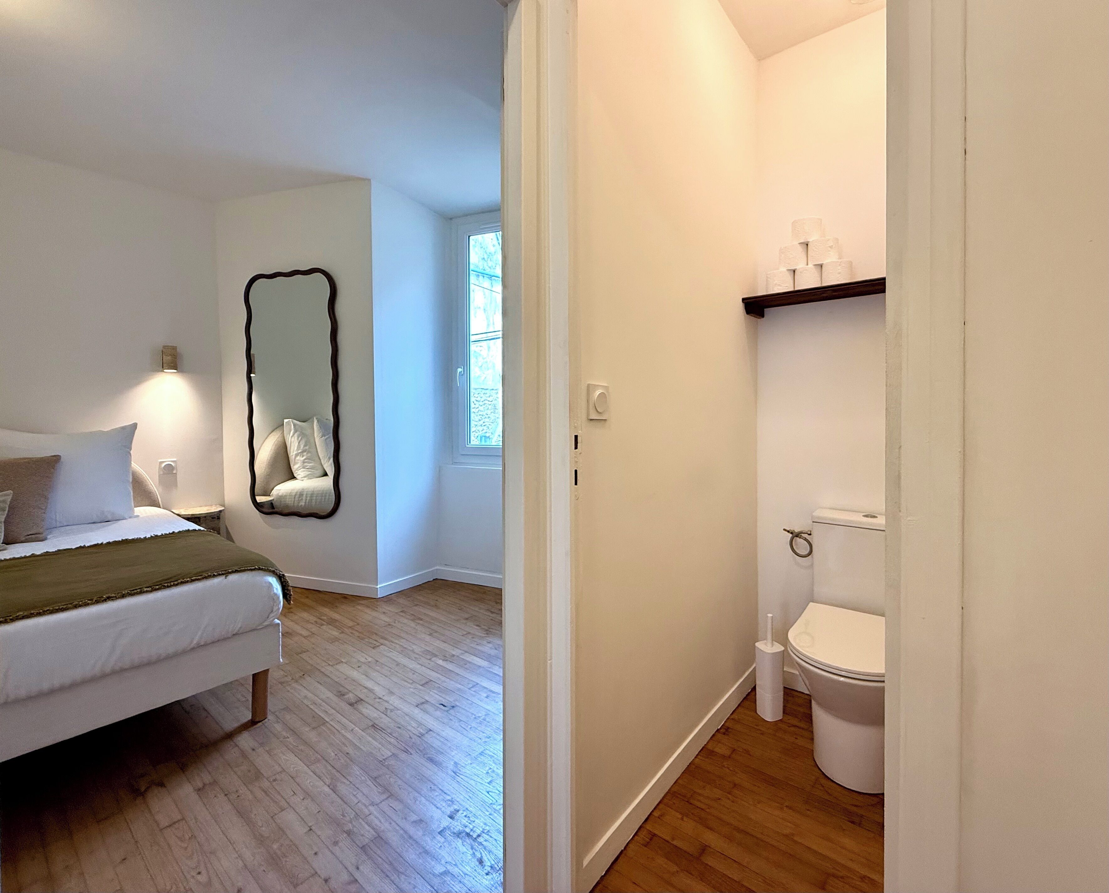 Een slaapkamer met een bed, een spiegel en een raam. De badkamer heeft een toilet, een wastafel en een spiegel.