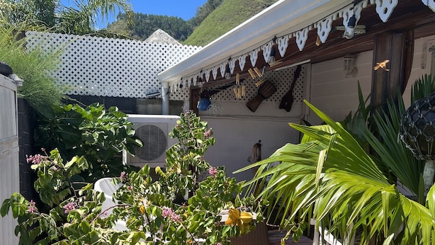 Um deck de madeira com cerca branca, uma árvore com flores cor-de-rosa e uma tenda branca com detalhes decorativos.