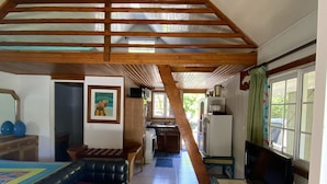 Uma sala ampla com uma cama mezanina, um sofá, uma televisão e uma cozinha ao fundo.