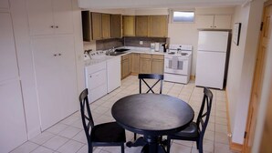 A compact kitchen with white cabinets, a stove, a sink, and a dining table with chairs. - Lake Cabin on North Long Lake (Brainerd)