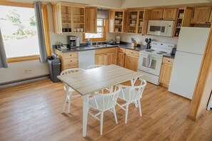 Une cuisine avec des meubles de rangement en bois, un four à micro-ondes, une cuisinière et un réfrigérateur. On y trouve également une table à manger avec des chaises.