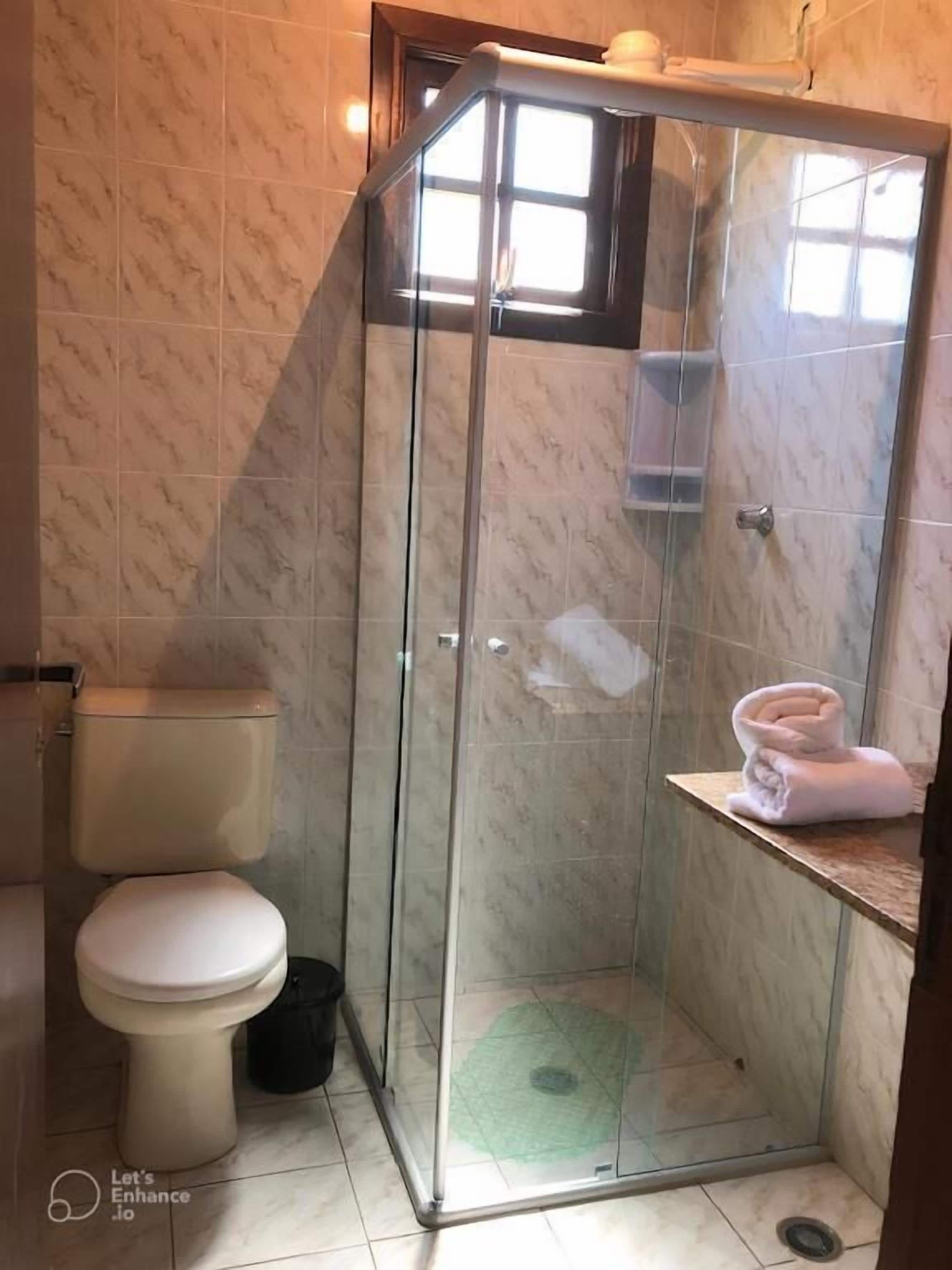 Un bagno con doccia vetro, water e portasciugamani.