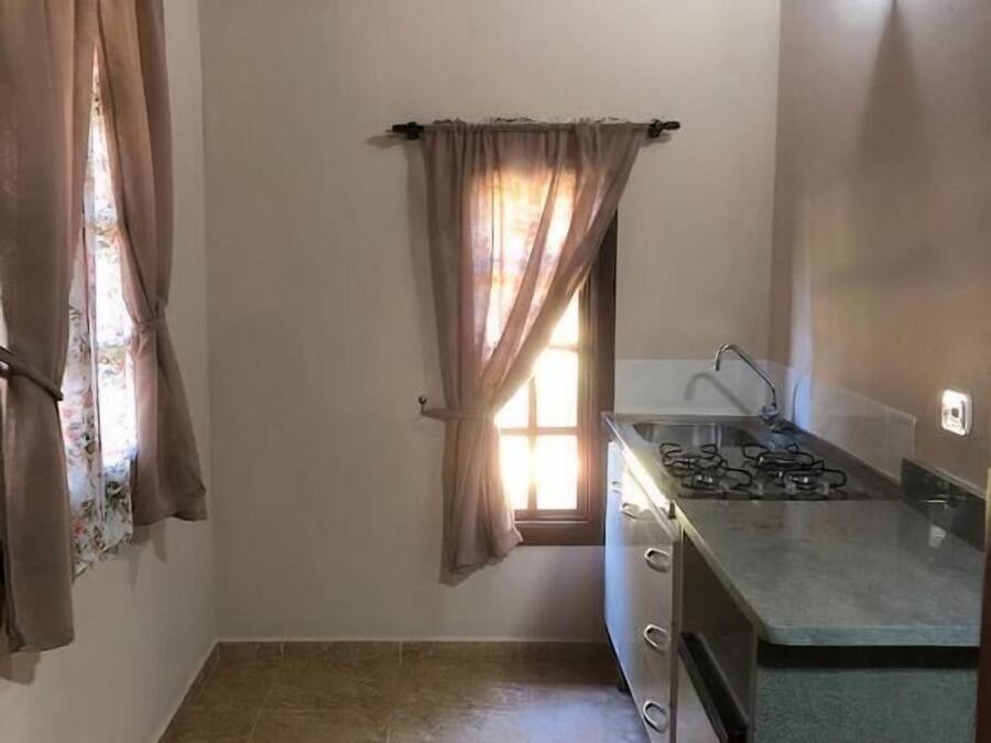 A small kitchen with a gas stove, a window with curtains, and a tiled floor.