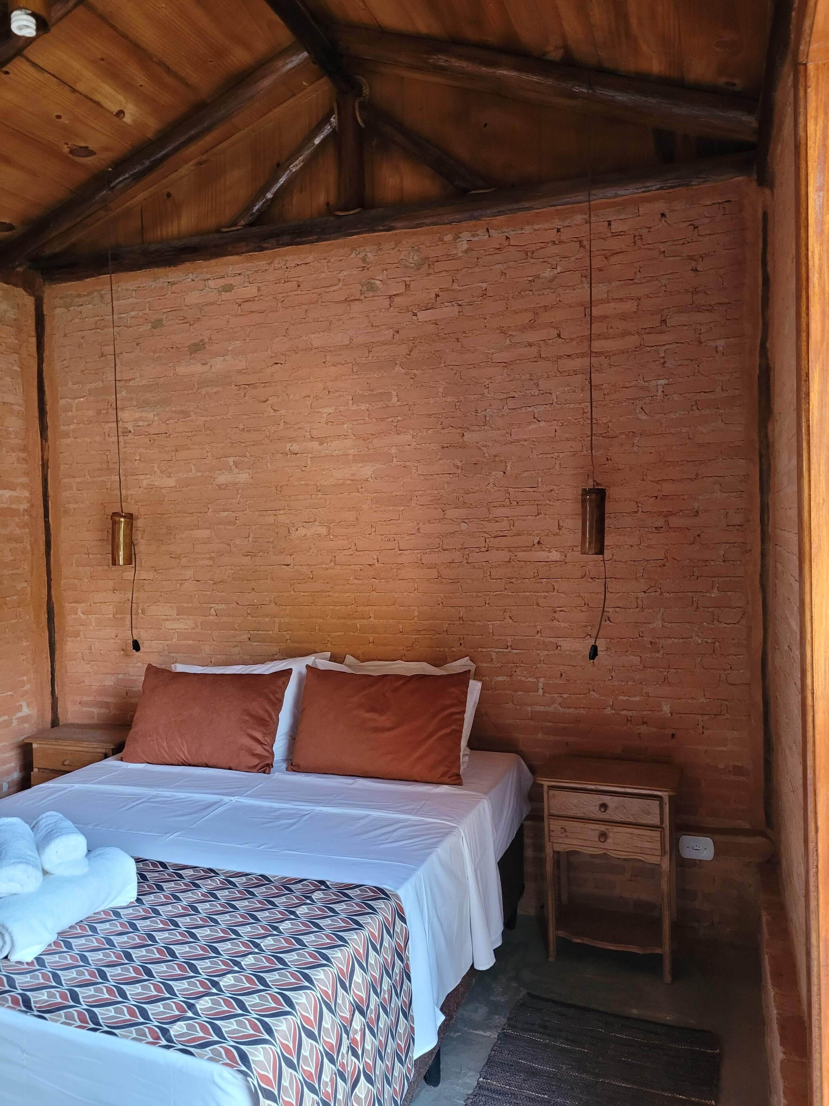 A room with a bed, a nightstand, a wooden dresser, and a brick wall.