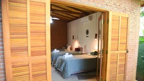 A room with two beds, wooden shutters, a brick wall, and a ceiling fan. - Pousada Realeza (Atibaia)