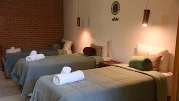 A hotel room with two beds, each with a green bedspread and white towels. There is a brick wall on one side and a white wall with a decorative plate on the other.