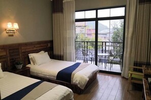 A hotel room with two beds, a balcony with a table and chairs, and a view of buildings outside. - Dongshan Yunju Hotel (Deqing)