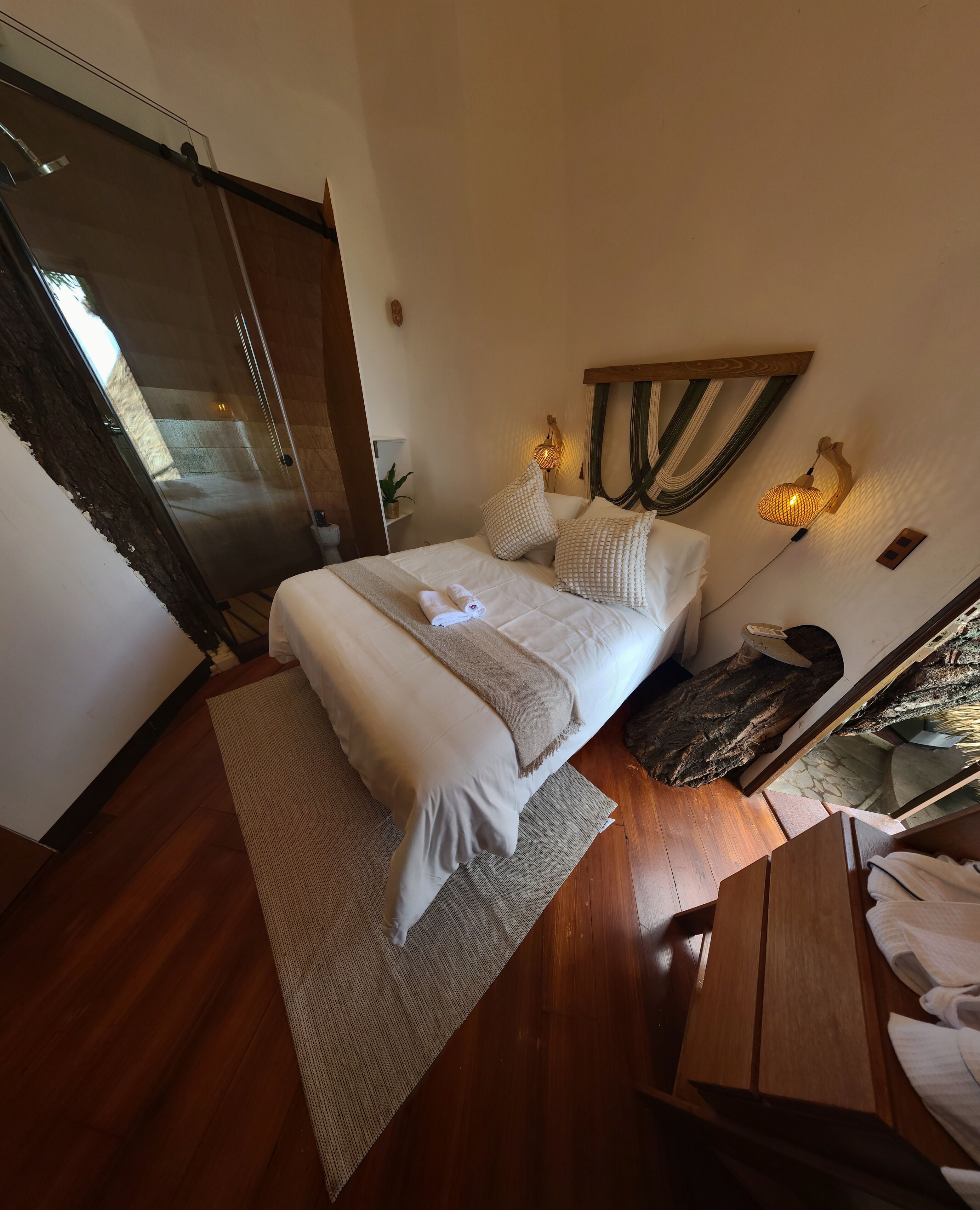 A bedroom with a bed, bedside tables, a nightstand, a mirror, a window with curtains, and a wooden floor.