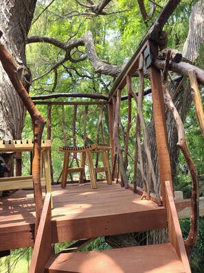 Une terrasse en bois avec un banc et une table, entourée d’arbres.