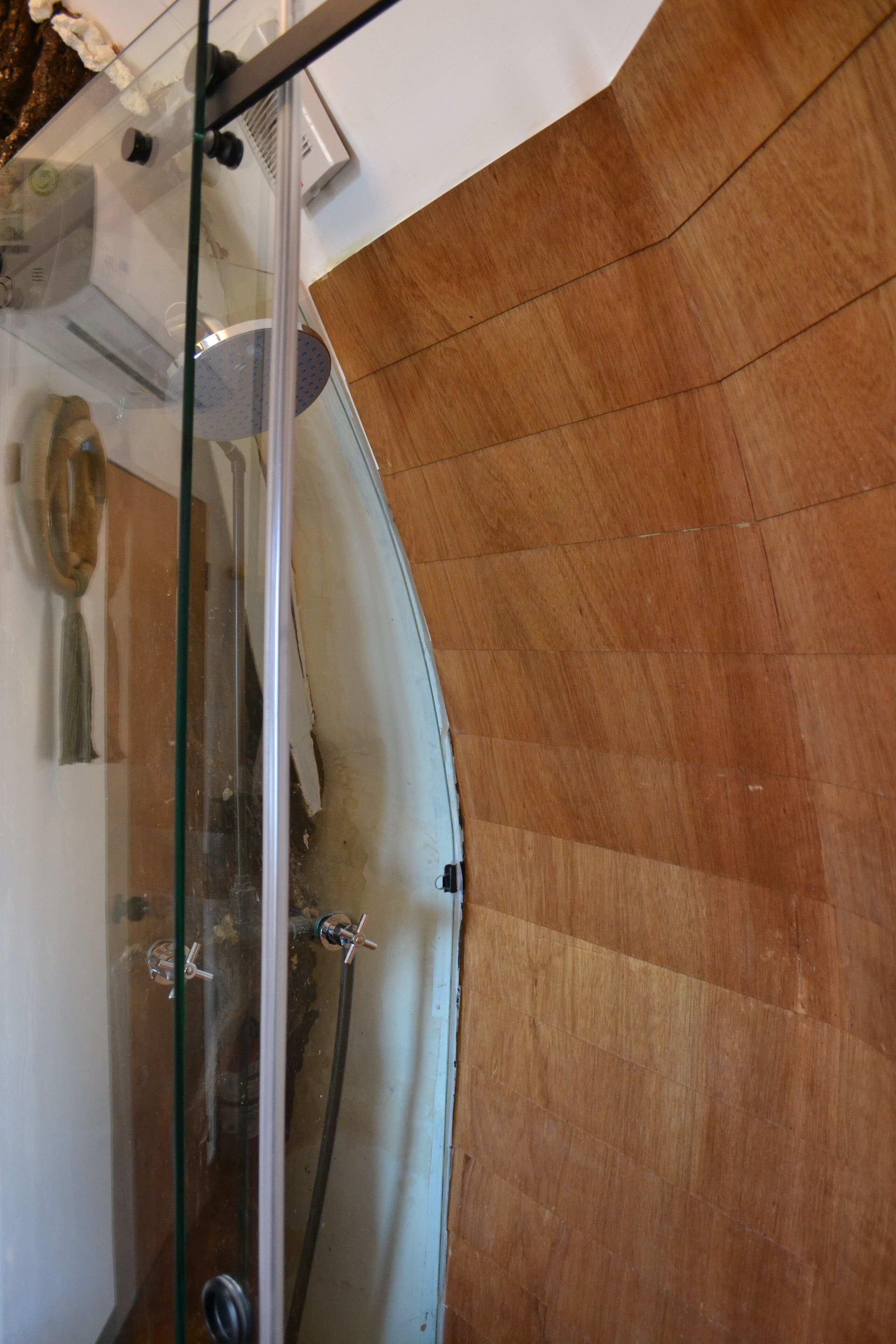 A shower area with a glass door, wooden walls, and a visible showerhead.