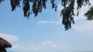 A thatched-roof structure with a view of a calm lake and distant mountains.
